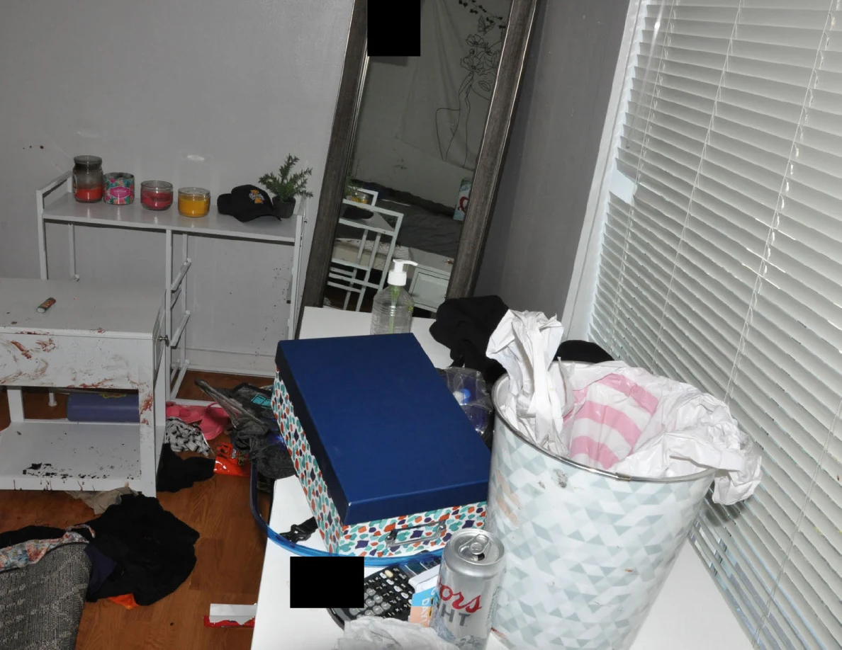 Desk with patterned wastebasket and boxes beside a tall mirror and white cabinet.