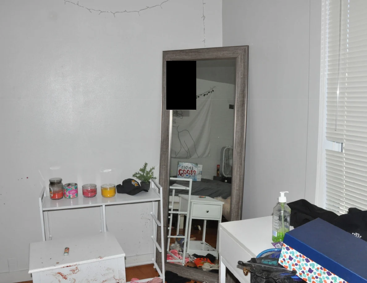 Tall mirror beside a white cabinet with candles, cap and small plant.