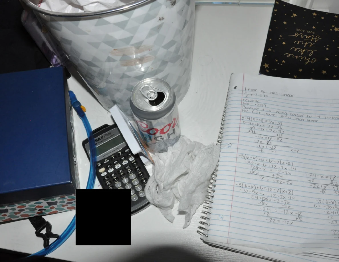 Calculator, drink can, tissues and open handwritten notebook on a white desktop.
