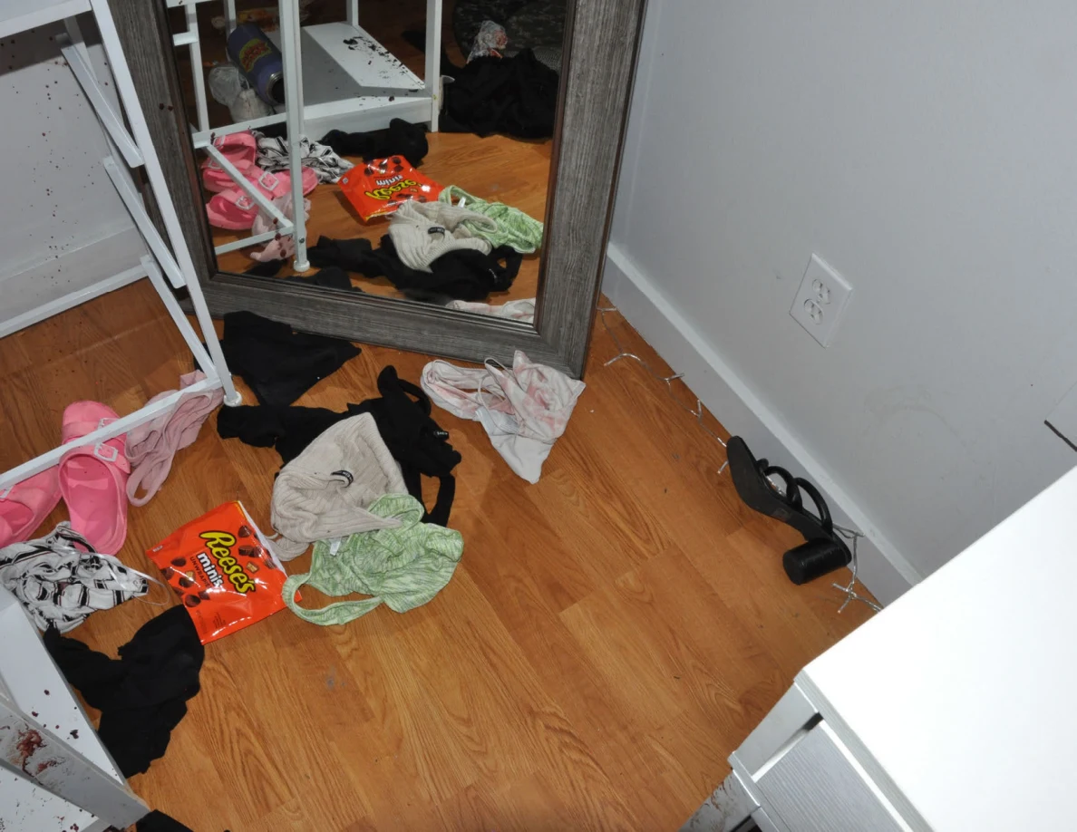 Clothing, pink slides and an orange snack wrapper on the floor beside a mirror.