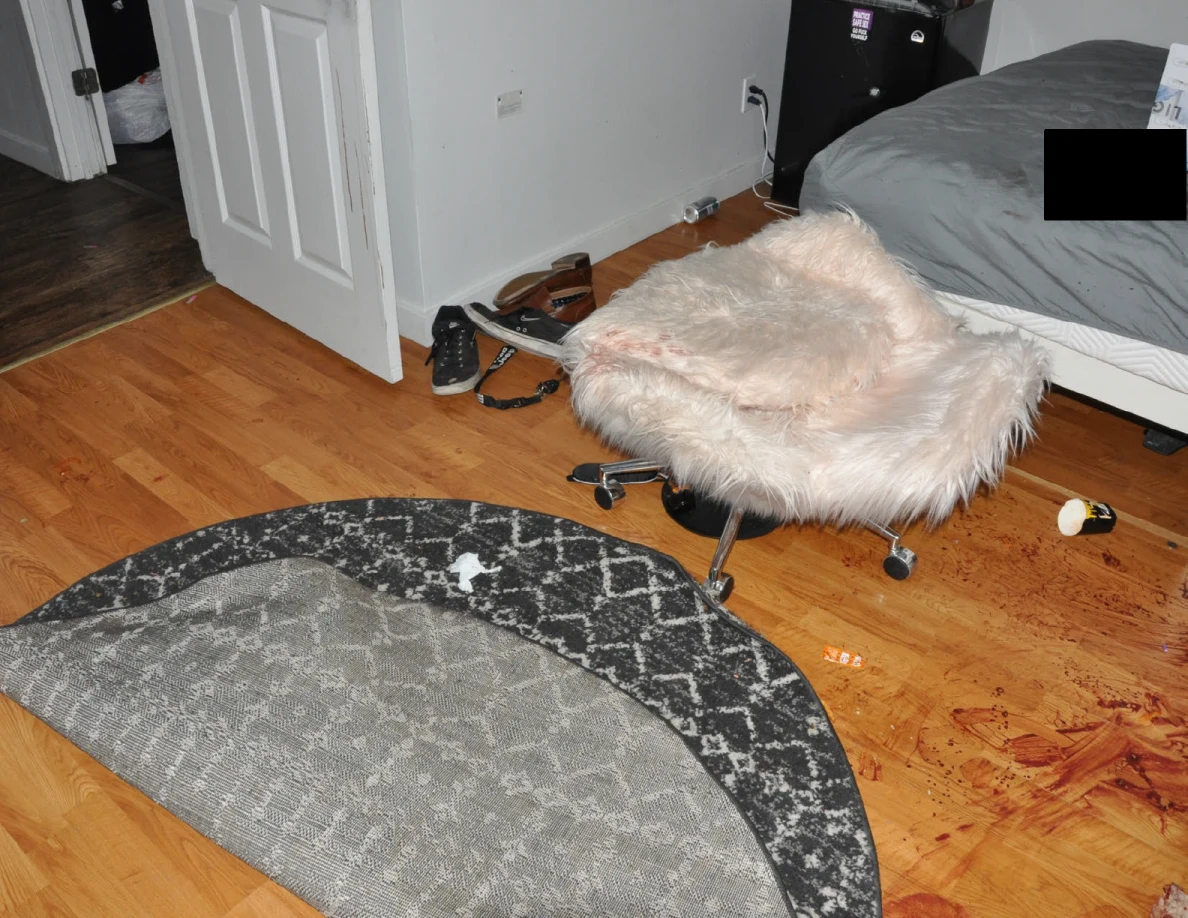 Fluffy pale chair between an open door and partly redacted bed beside a folded rug.