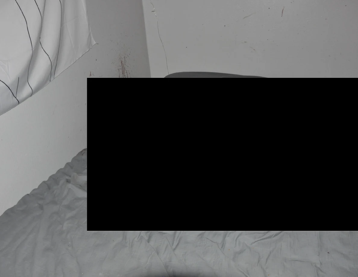 Gray bedding beneath a large black redaction with reddish wall marks visible above.