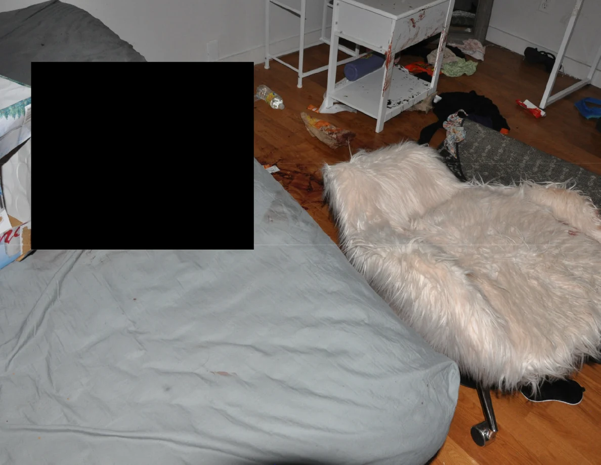 Partly redacted bed beside a fluffy chair, folded rug and white furniture.