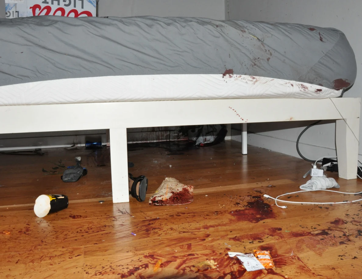 Gray sheet and white bed frame with reddish marks above a marked floor.