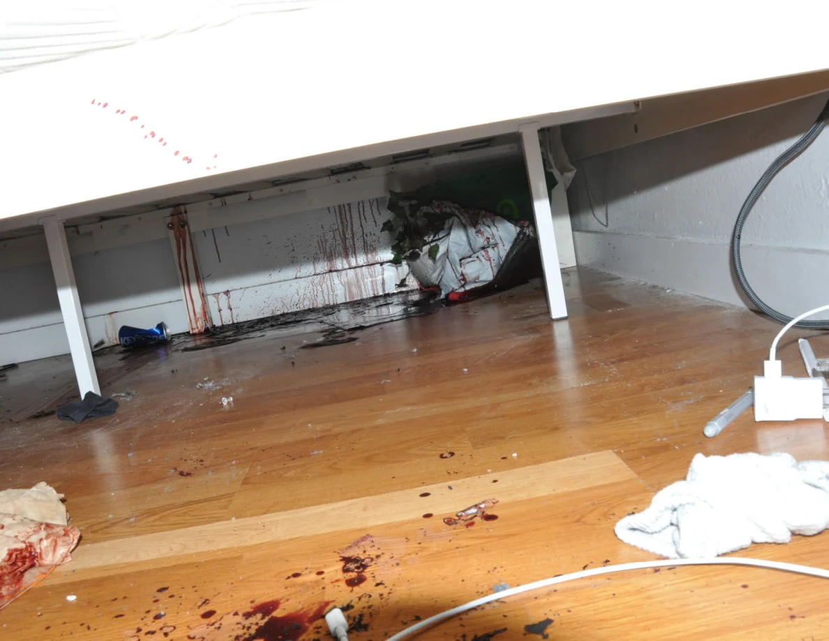 Under-bed view with reddish wall streaks, a bag and white power cables.