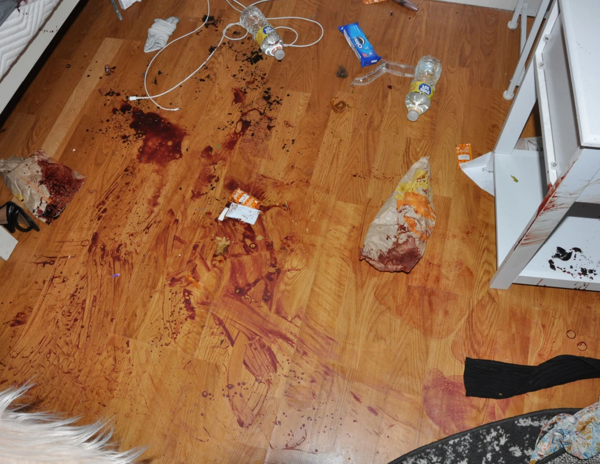 Reddish floor streaks among cables, bottles, wrappers and clothing.