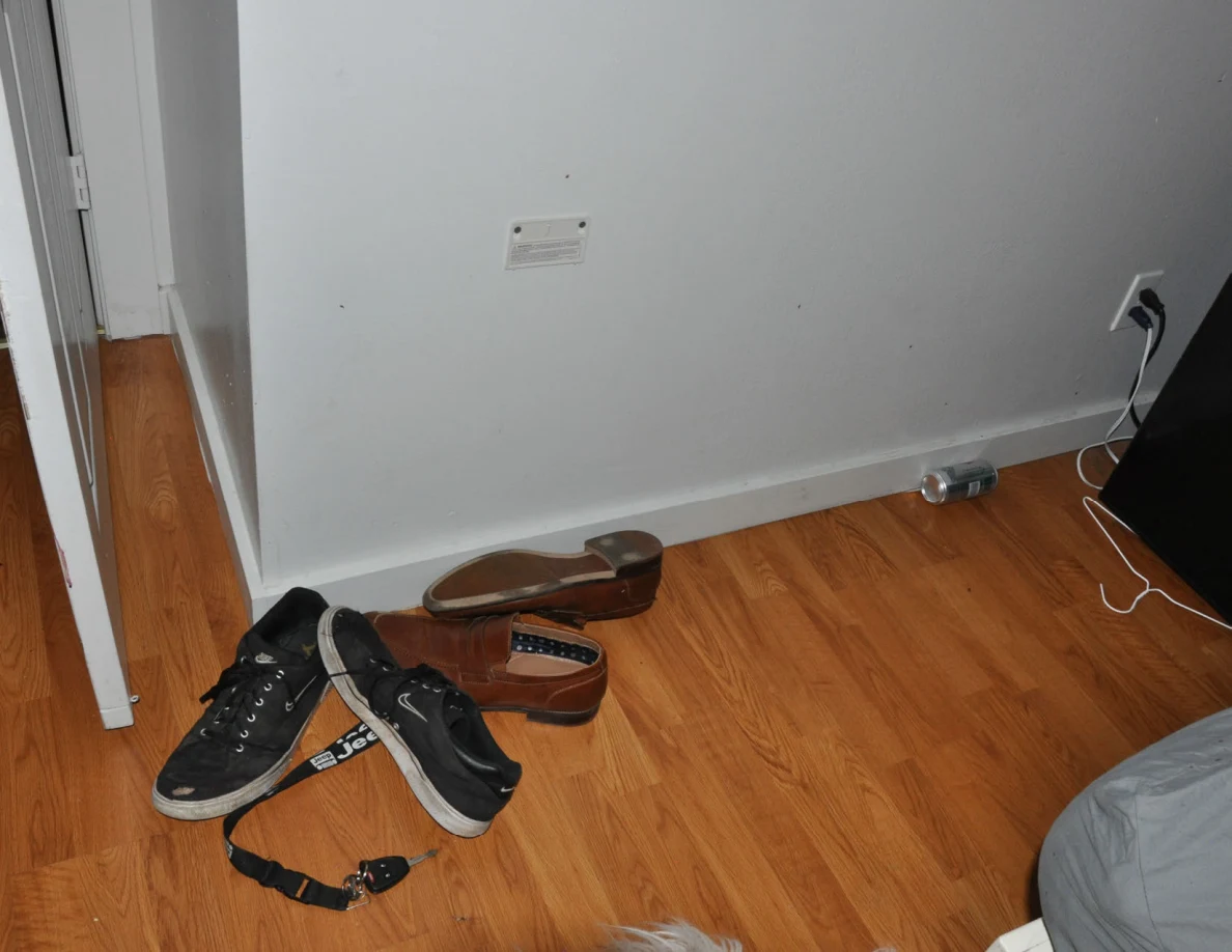 Footwear and a strap below a white wall beside a mini fridge cable.