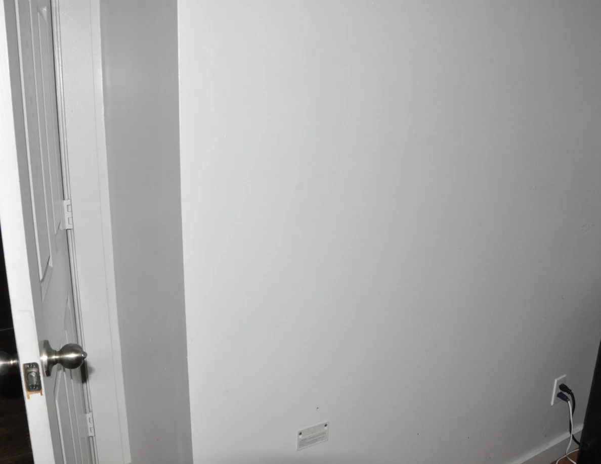 White bedroom wall beside an open door and outlet.