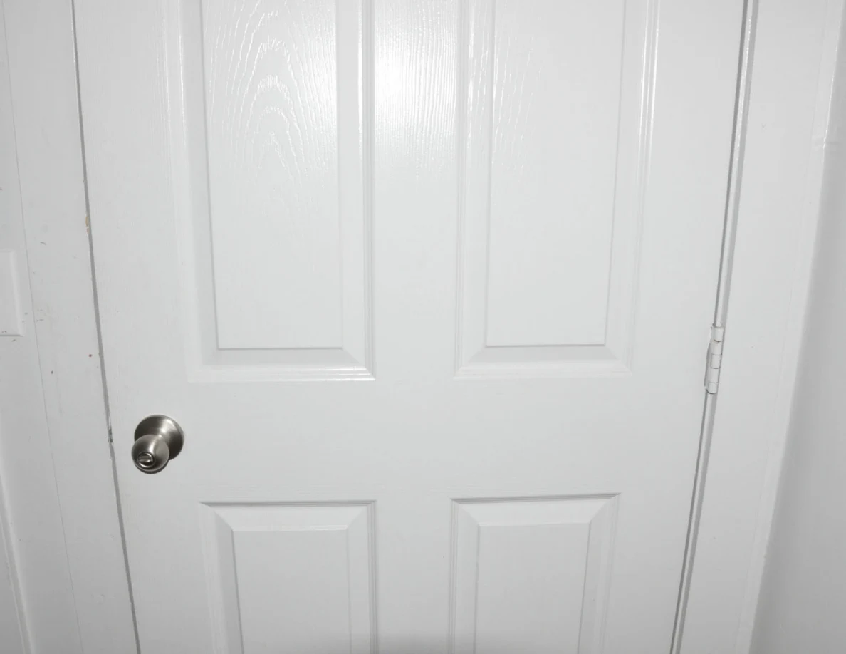 Middle panels and round metal knob of a closed white door.