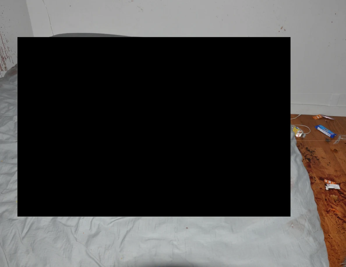 Gray-covered bed largely obscured by a black redaction beside reddish floor marks.