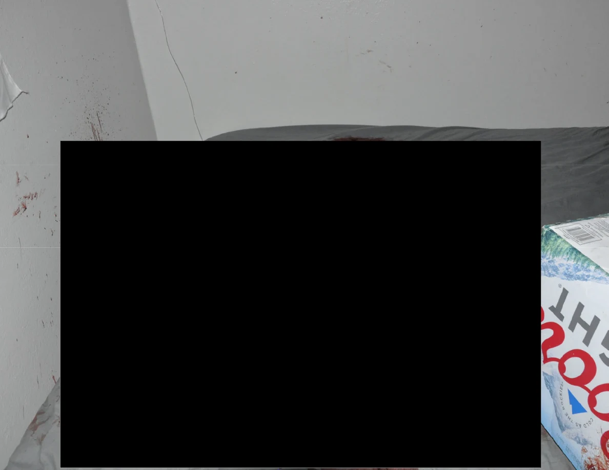 Partly redacted bed beside a beverage carton and reddish wall marks.