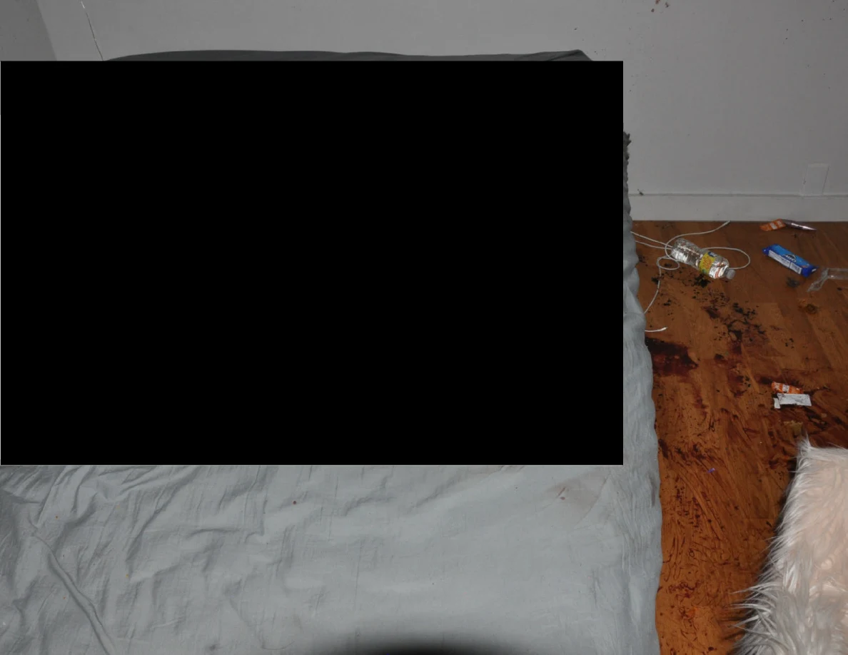 Partly redacted bed beside cables and reddish floor marks.