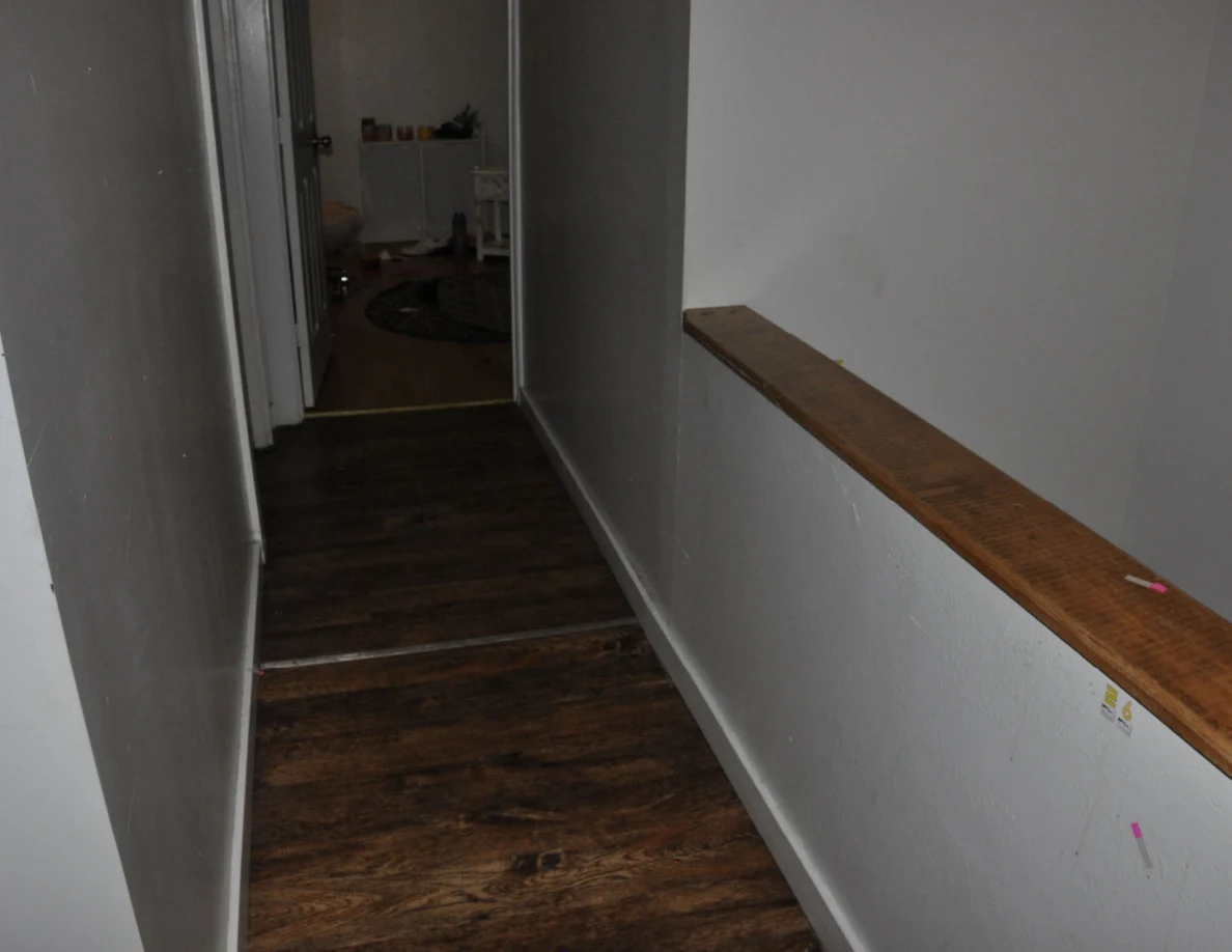 Hallway flooring beside a wooden stair rail and small markers.
