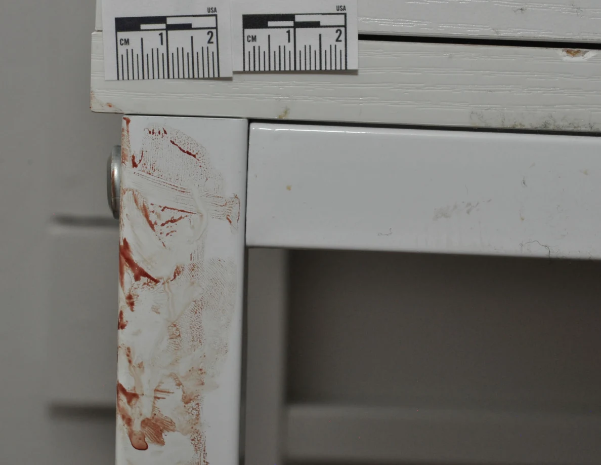 Measuring scales above reddish smears on a white desk leg.