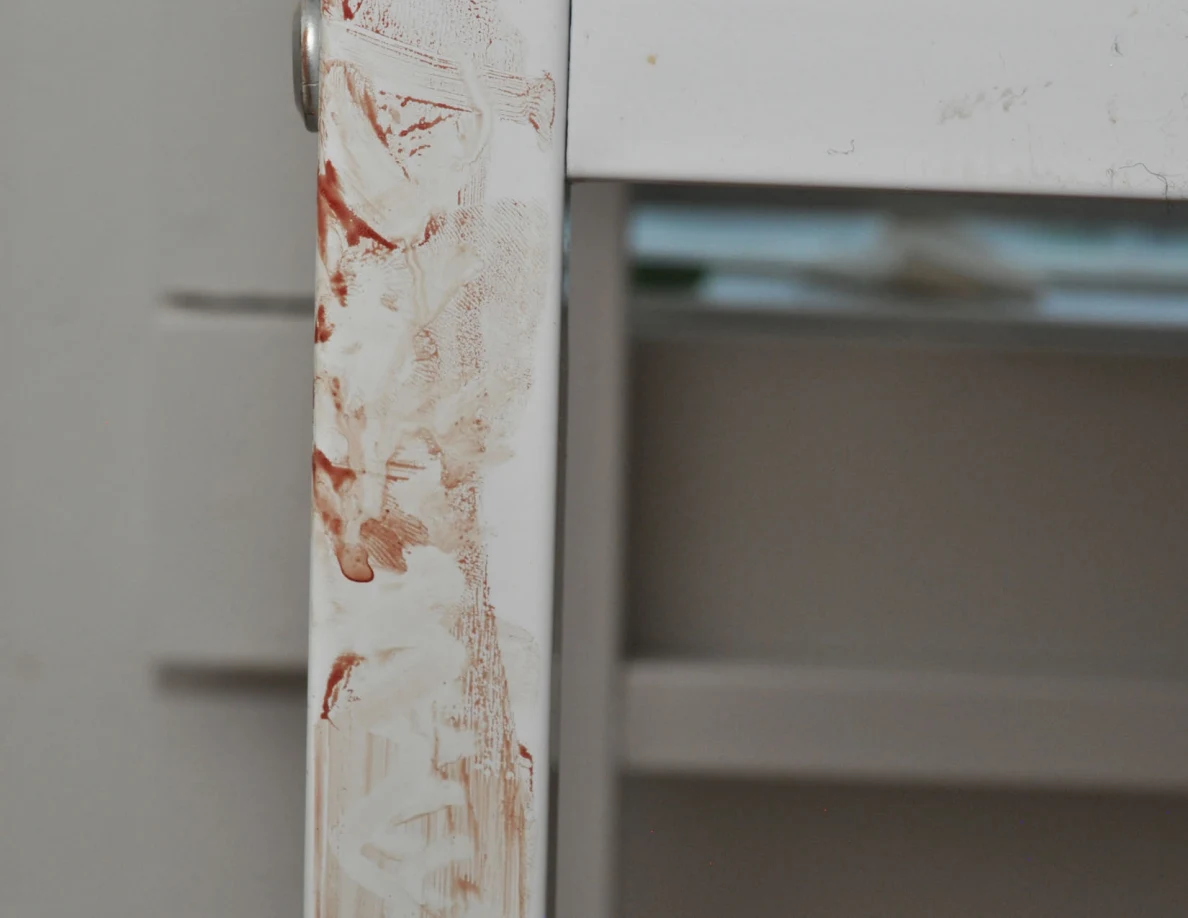 Close view of reddish smears on a white desk leg.