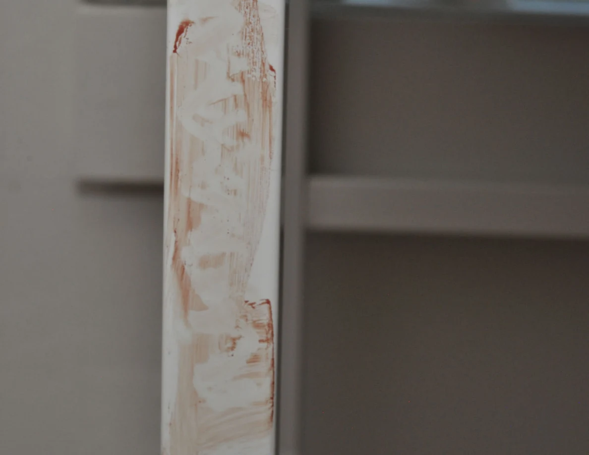 Close view of pale reddish streaks on a white desk leg.
