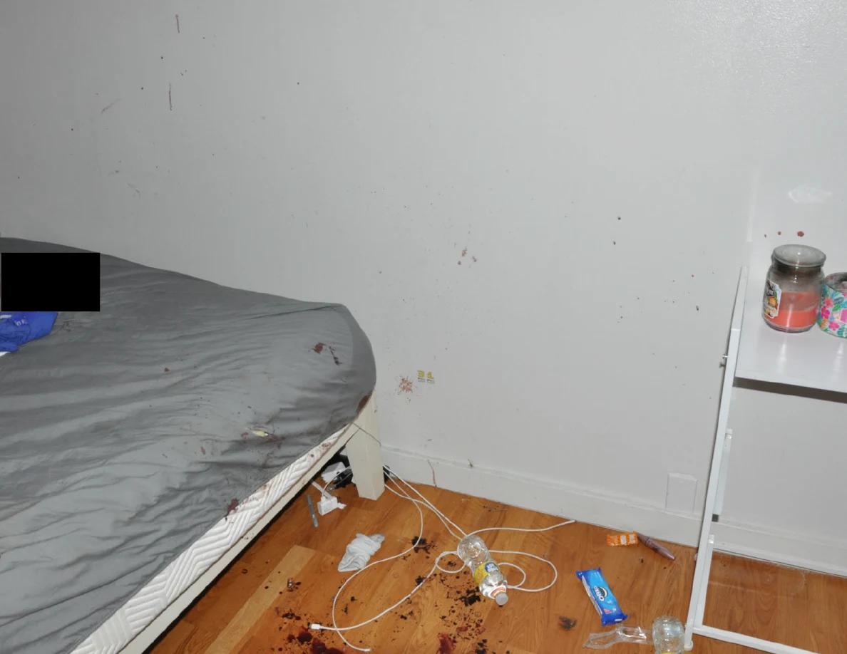 Bed beside a white wall with reddish spots and cables on marked flooring.
