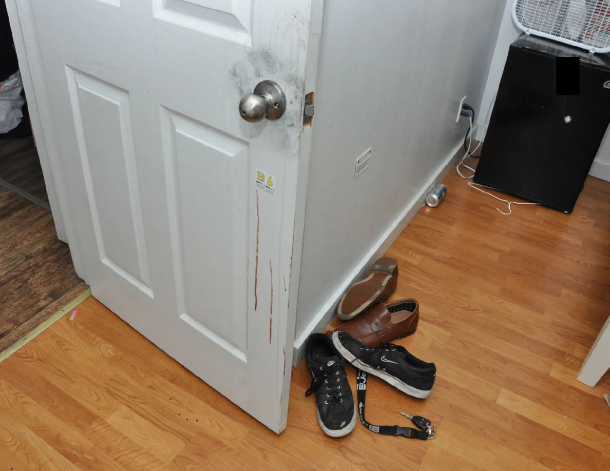 Open white door with reddish vertical streaks beside footwear and a mini fridge.