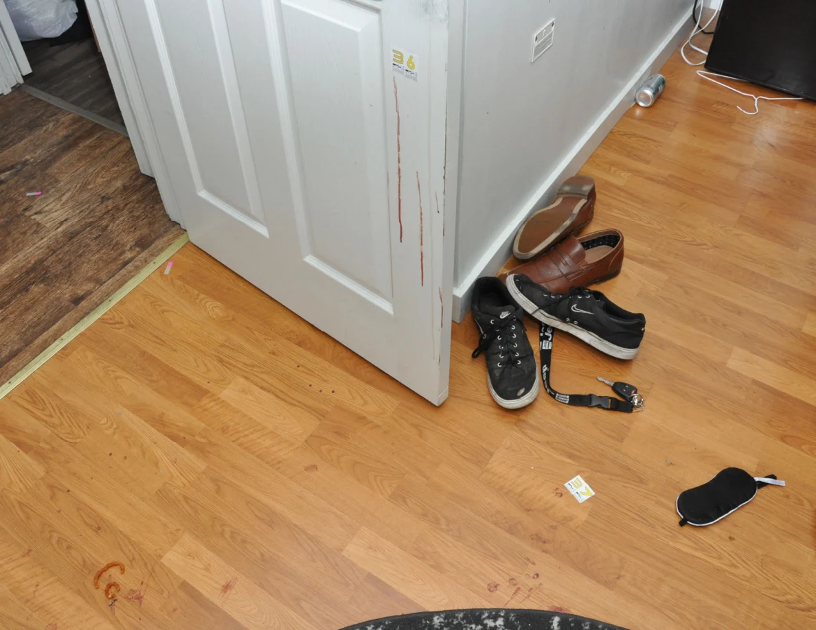 Footwear and floor marks beside an open white door with reddish streaks.