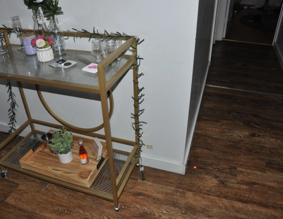Gold drinks cart with plants, flowers and glasses beside a hallway.