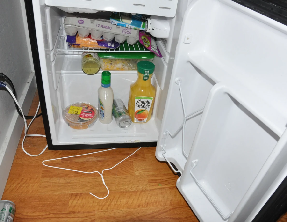 Open mini fridge containing eggs, bottles, packaged food and orange juice.