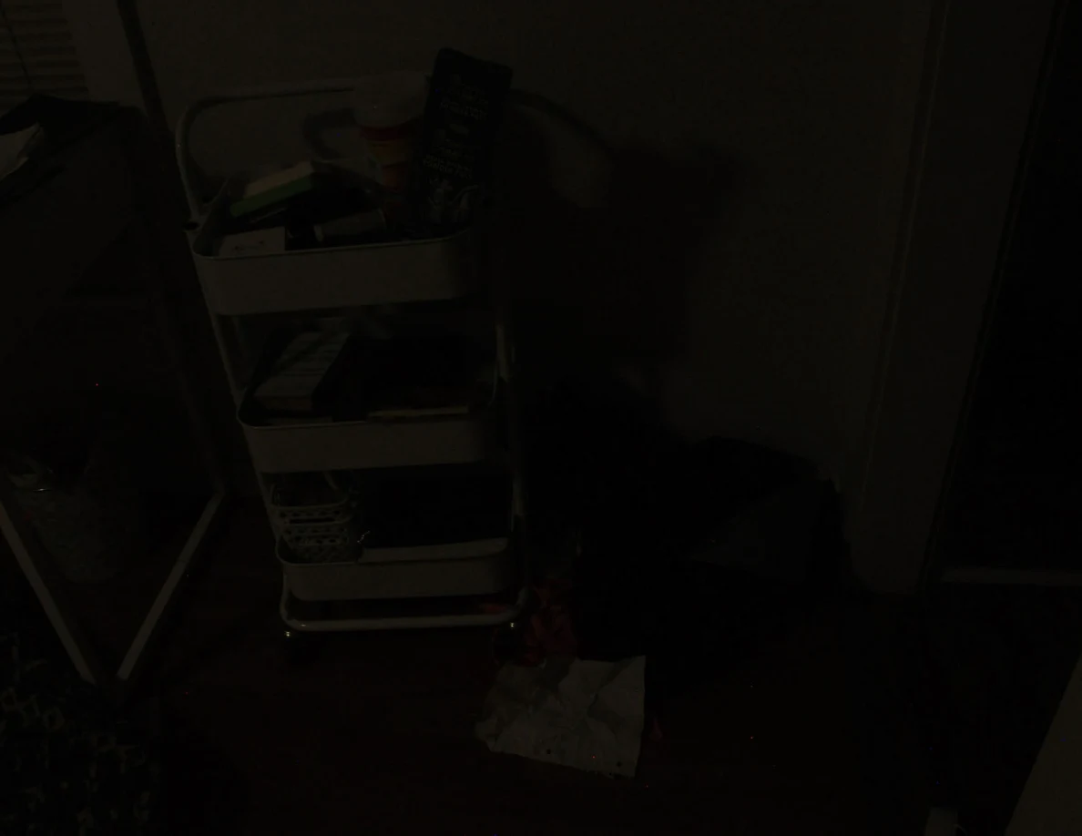 Very dim view of a rolling cart and clothing in a bedroom.
