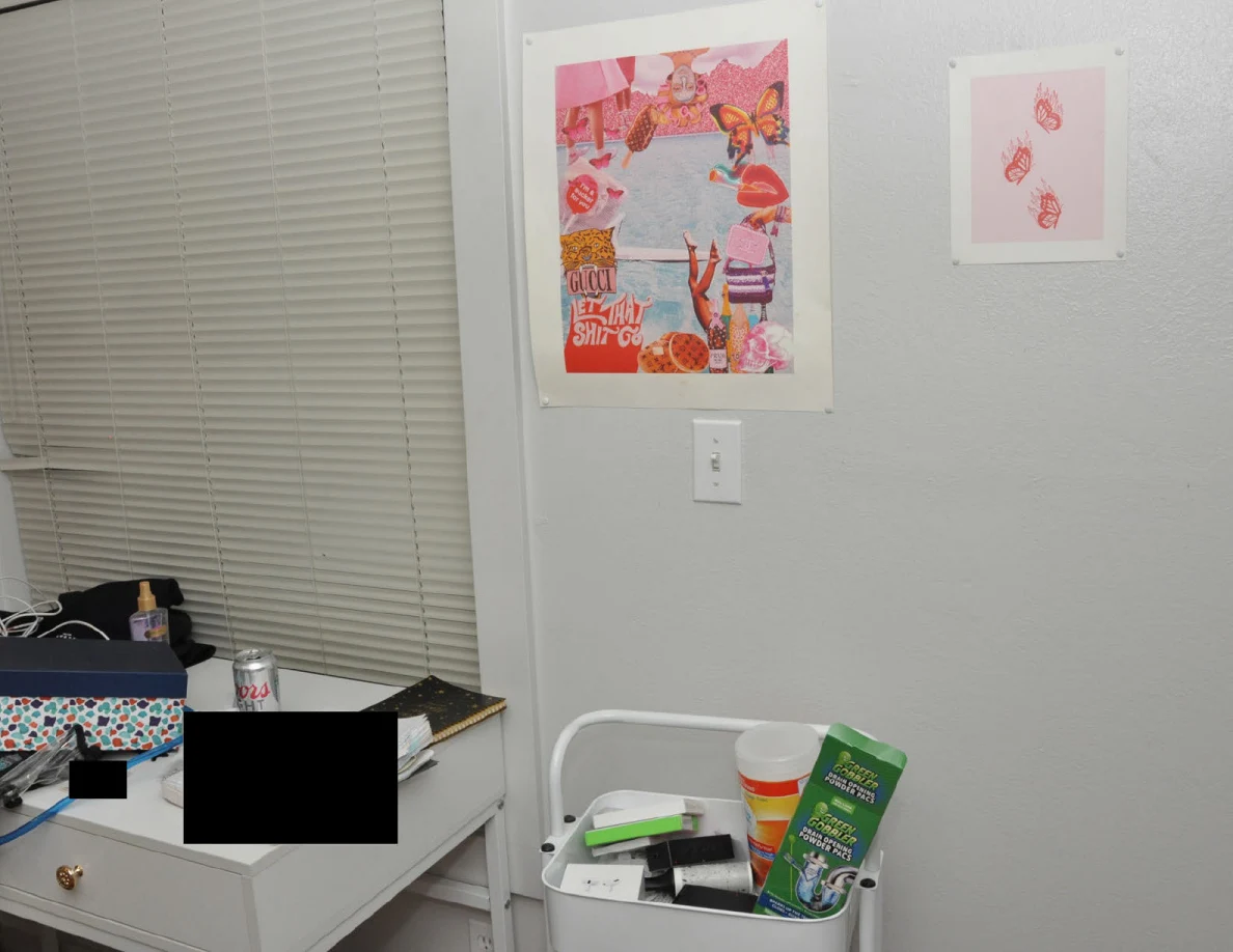 Pink wall prints above a rolling cart beside a partly redacted desk.