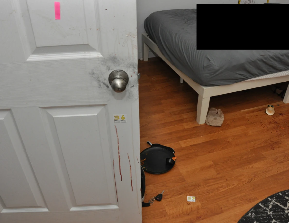 White door with pink tape and reddish streaks beside a partly redacted bed.