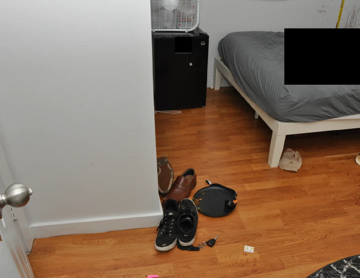 Footwear and a dark round object near the bed and mini fridge.