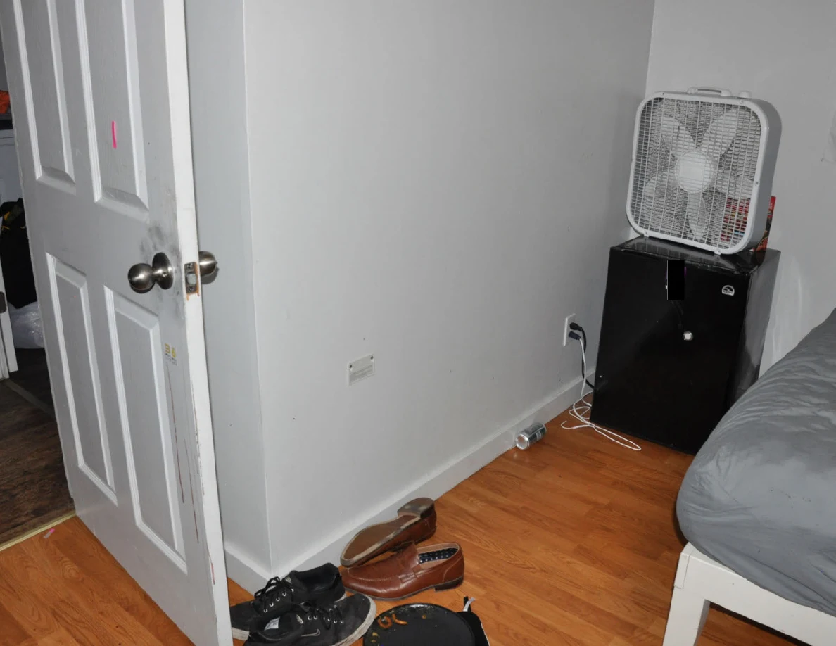 Open white door beside footwear and a box fan on a mini fridge.