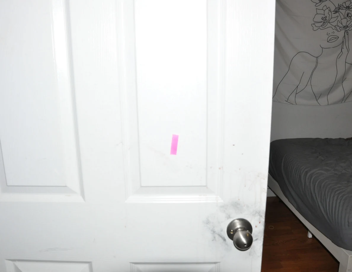 White door with pink tape and dark smudges around its metal knob.