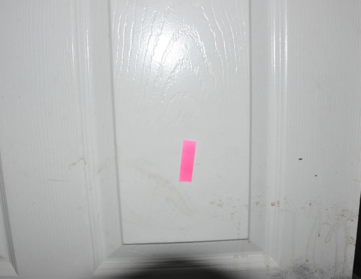 Close view of pink tape and pale smears on a white door.