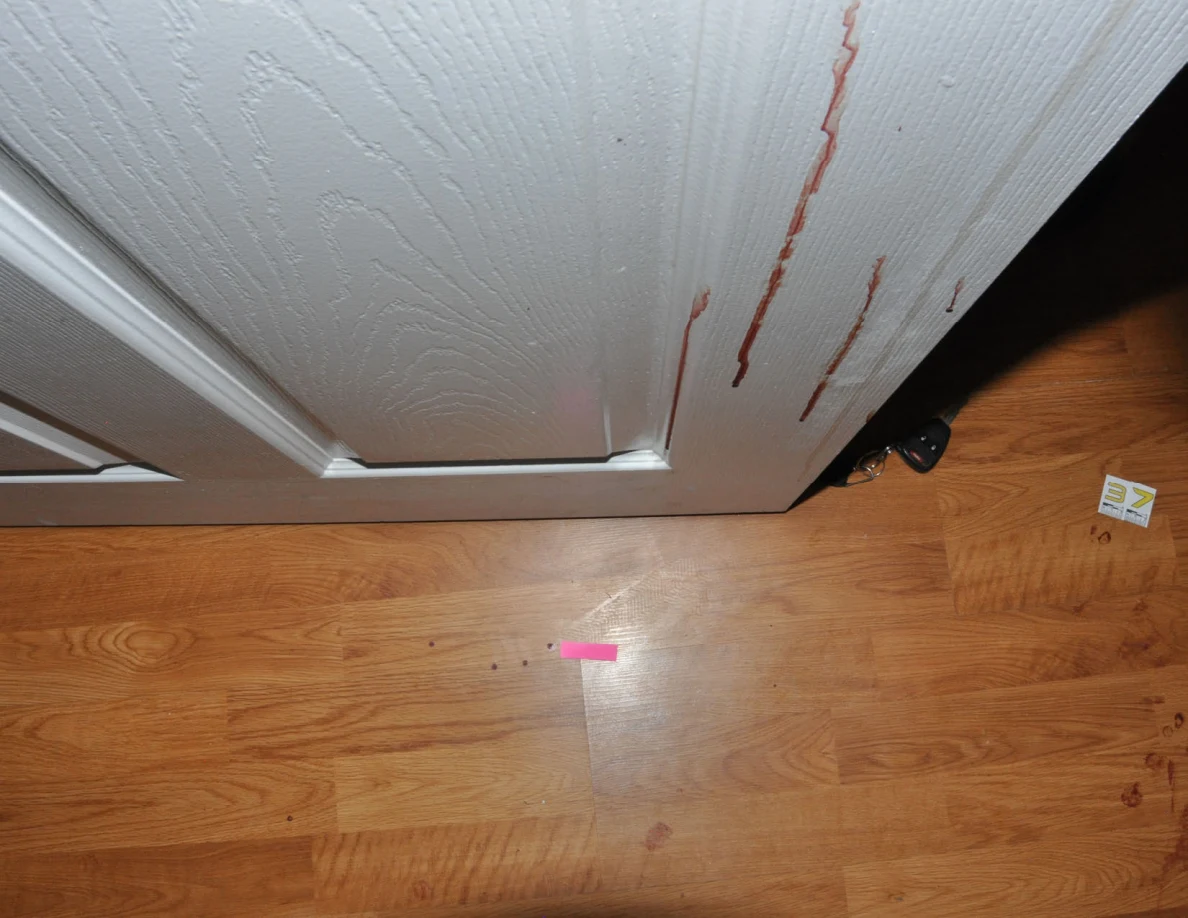 Pink tape on the floor beside a reddish-streaked door and floor scale label.
