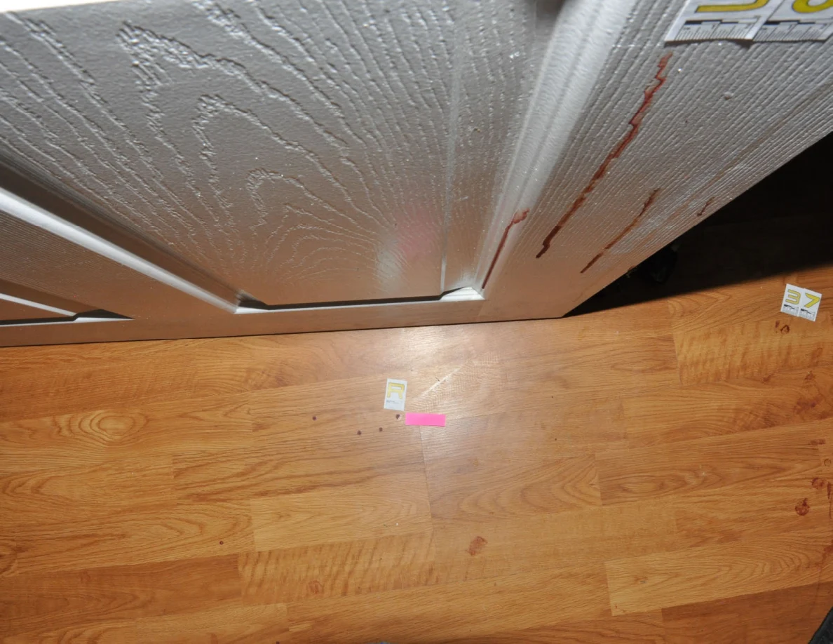 Floor markers and pink tape beside a white door with reddish streaks.