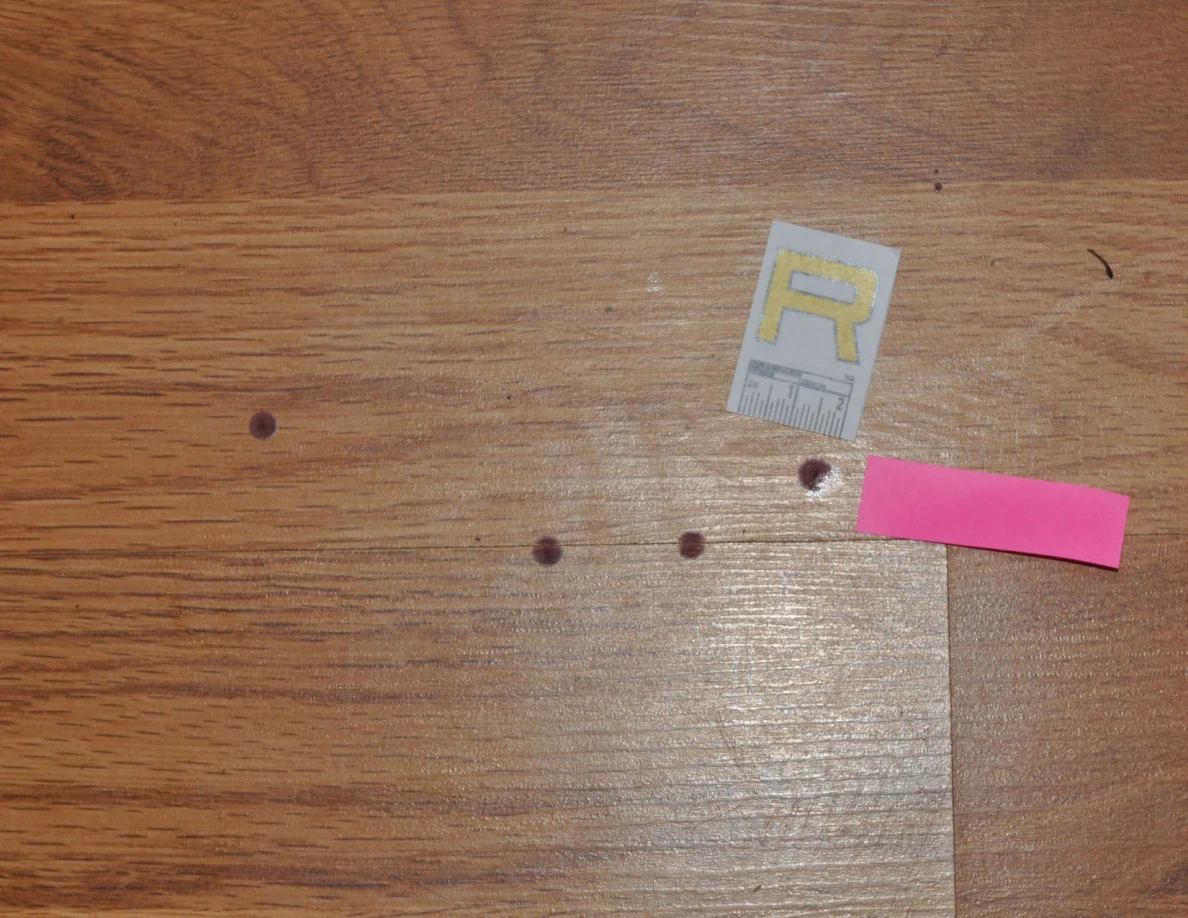 Close view of reddish floor spots beside scale label R and pink tape.