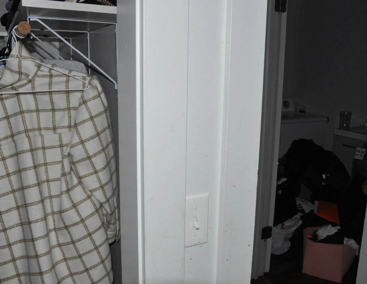 Closet doorway with hanging plaid clothing beside a wall switch.