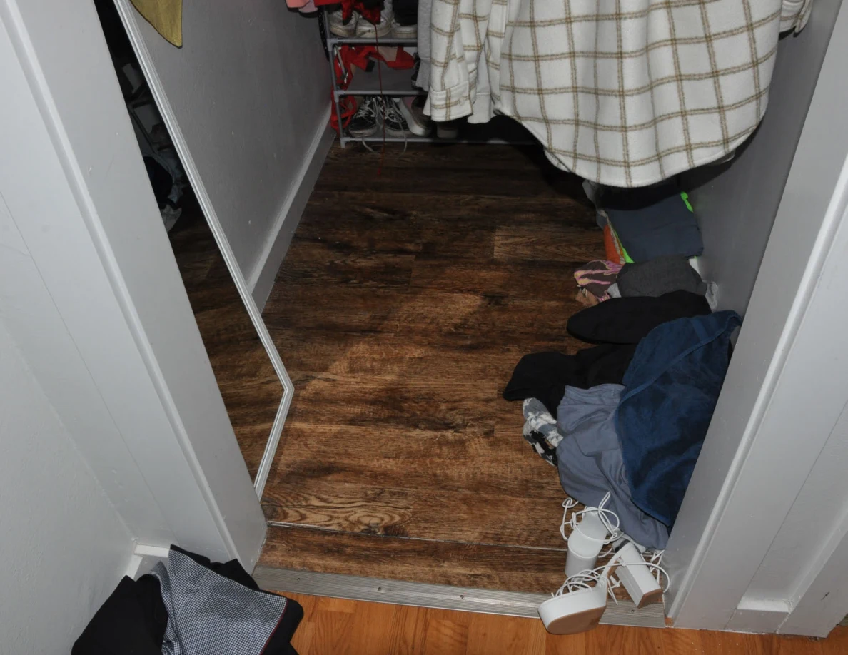 Walk-in closet with a mirror, hanging plaid clothing and scattered footwear.