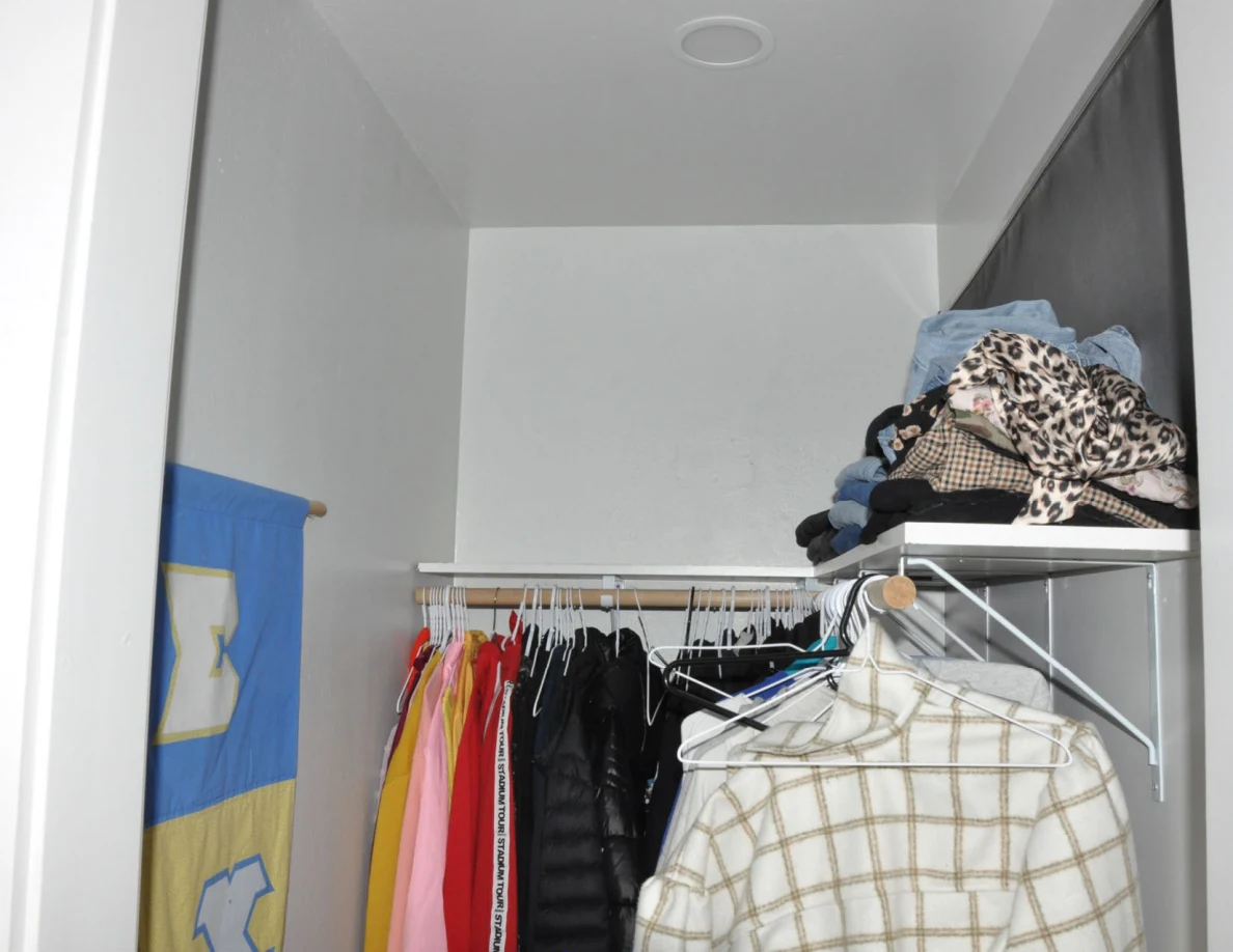 Upper closet shelves holding folded clothes above hanging garments.
