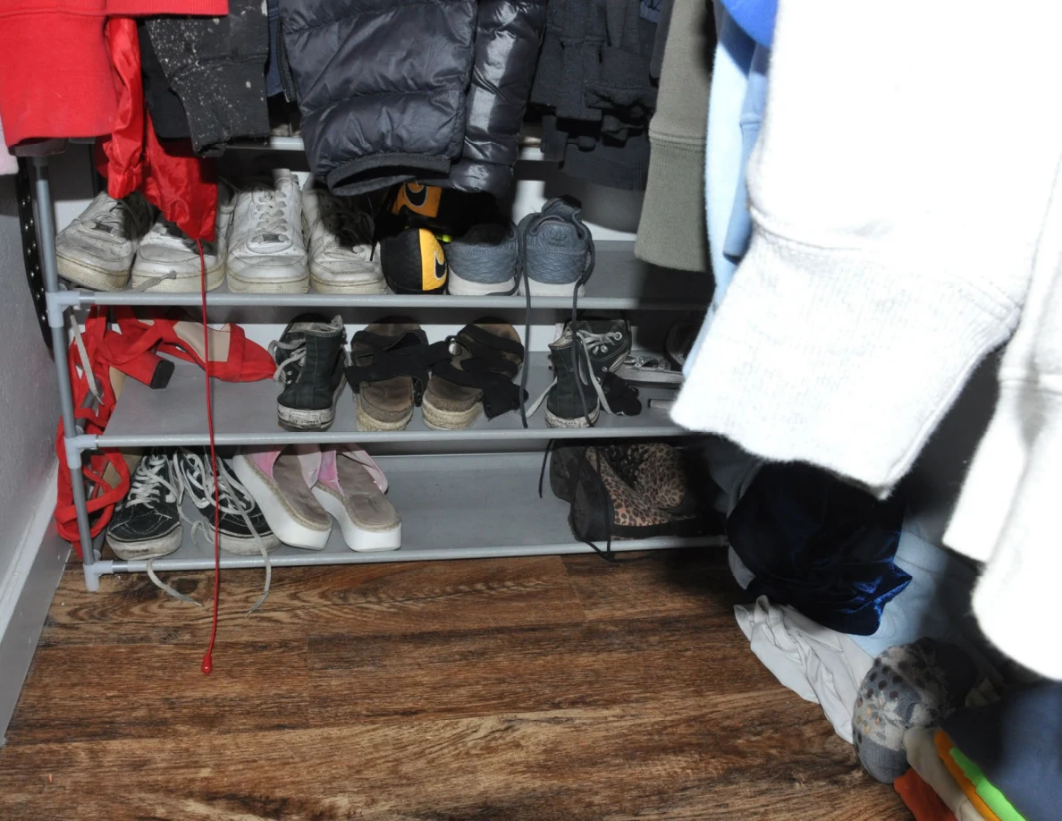 Multi-tier shoe rack beneath hanging closet clothing.
