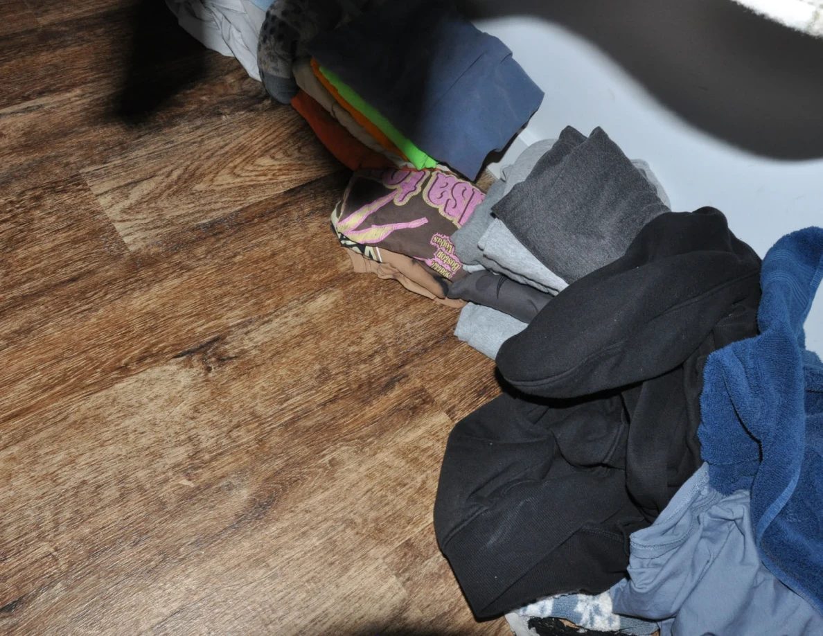 Folded clothing along the edge of a wood-pattern closet floor.