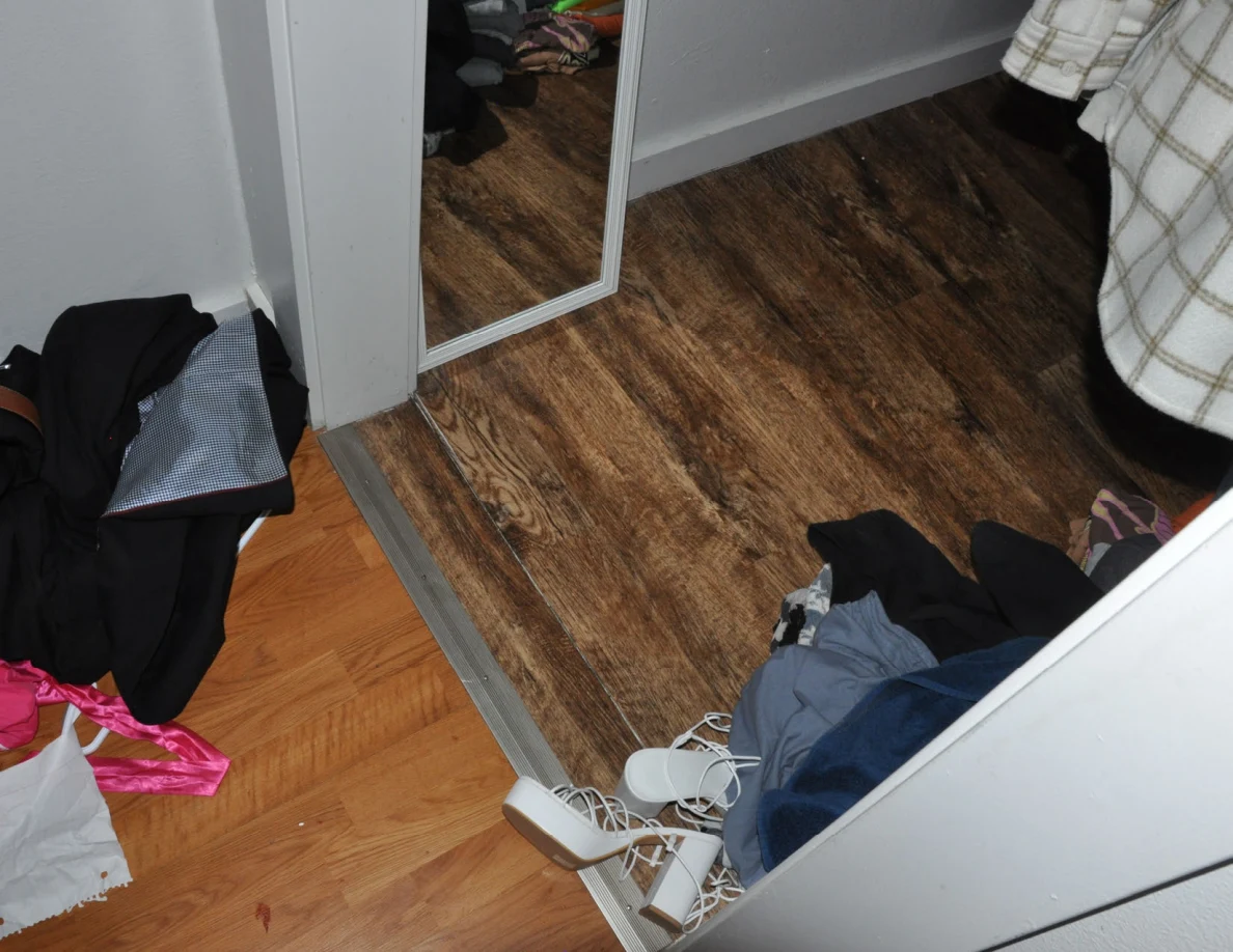Closet threshold with a tall mirror, scattered clothing and white strappy shoes.
