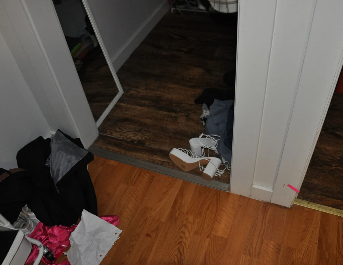 Closet doorway with white strappy shoes and clothing beside pink tape.