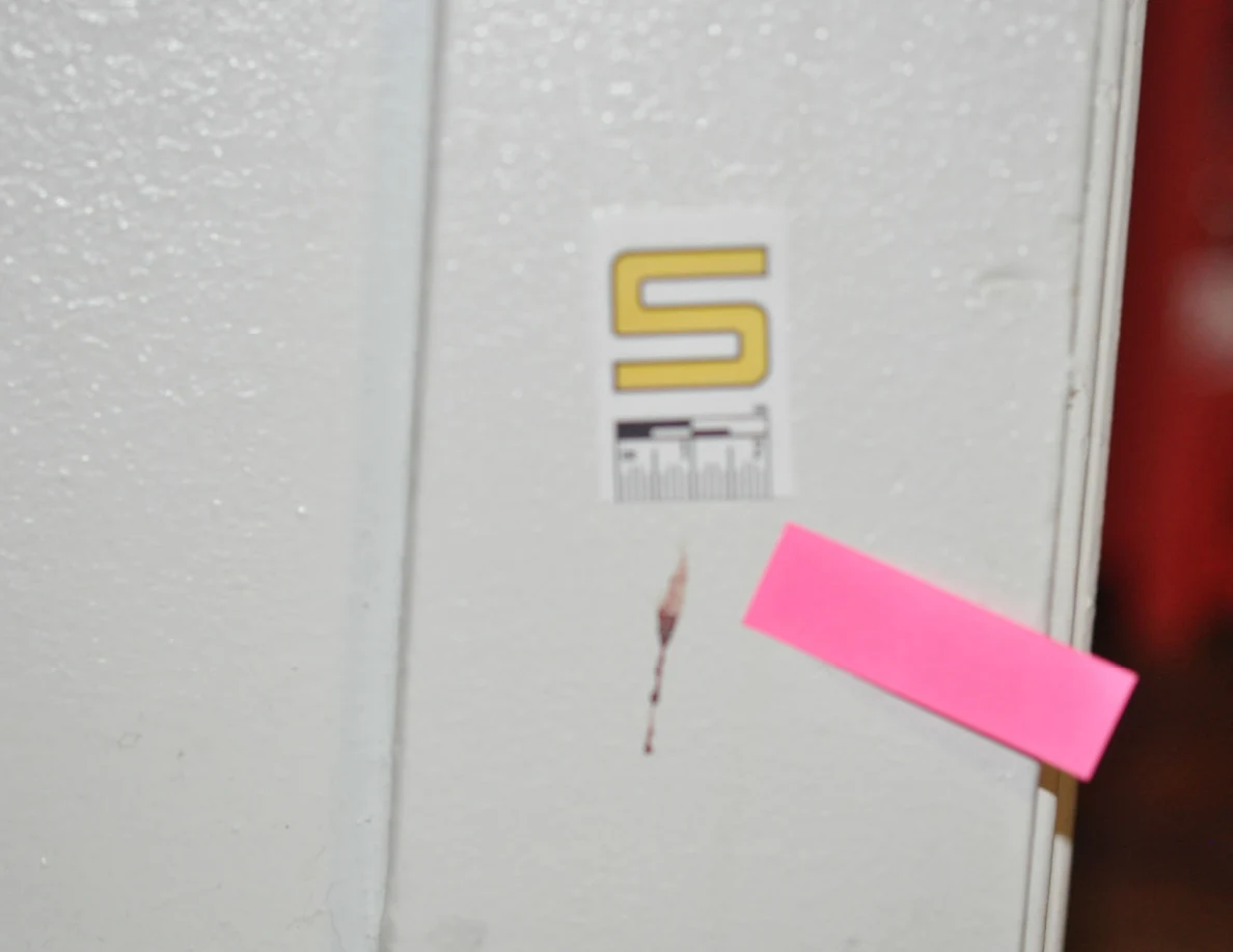 Close view of a reddish mark beside scale label S and pink tape on white door trim.