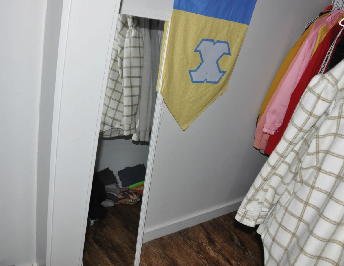 Closet mirror, hanging plaid garment and blue-and-yellow banner.