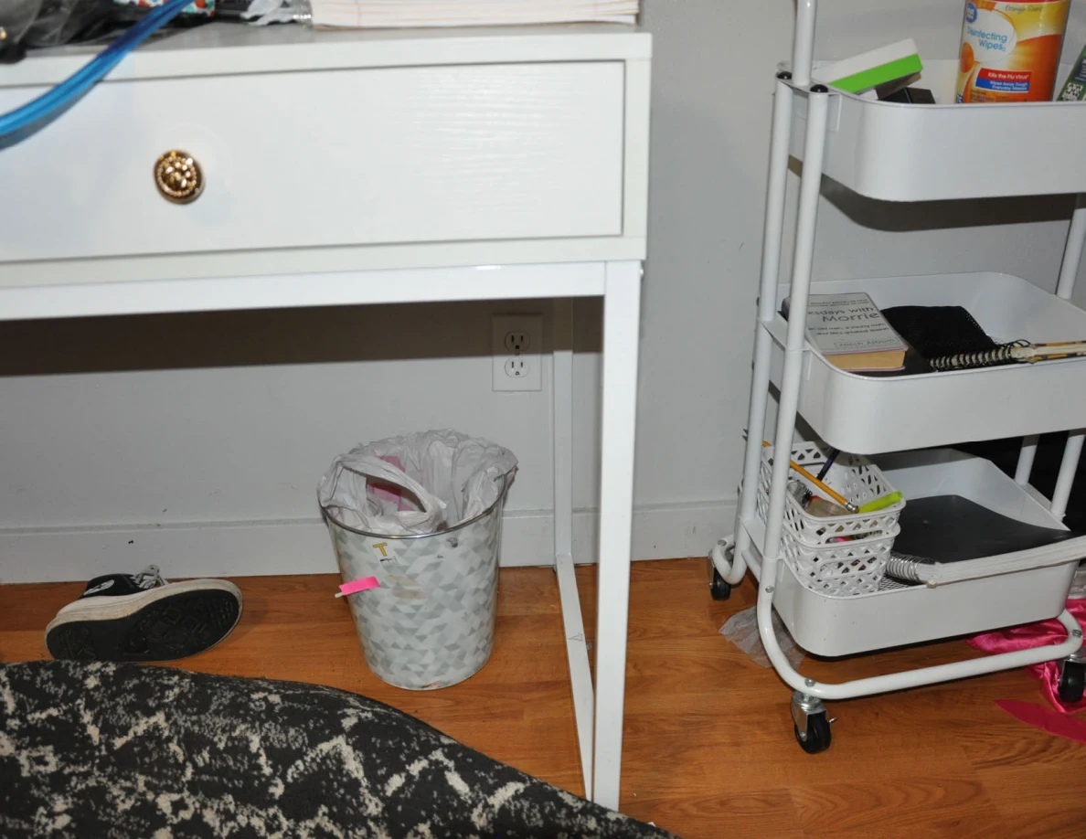 Patterned wastebasket with pink tape beneath a desk beside a rolling cart.