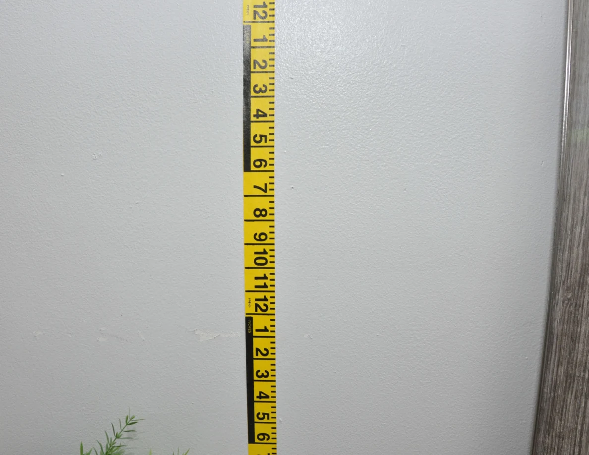 Vertical yellow measuring tape against a pale wall beside a mirror frame.