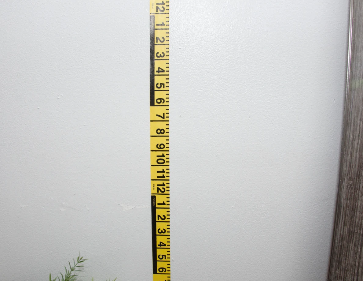 Vertical yellow measuring tape against a pale wall beside a mirror frame.