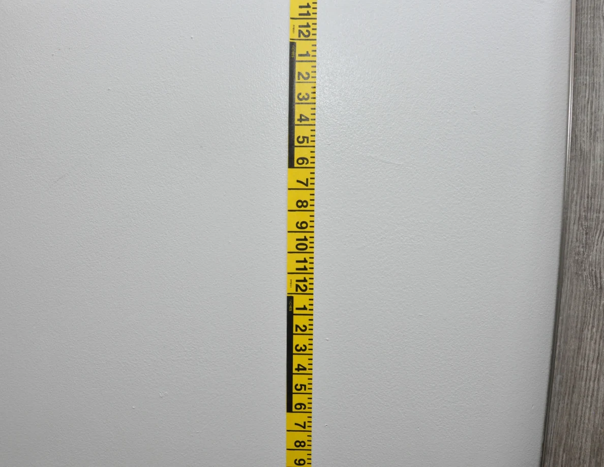 Vertical yellow measuring tape against a pale wall beside a mirror frame.