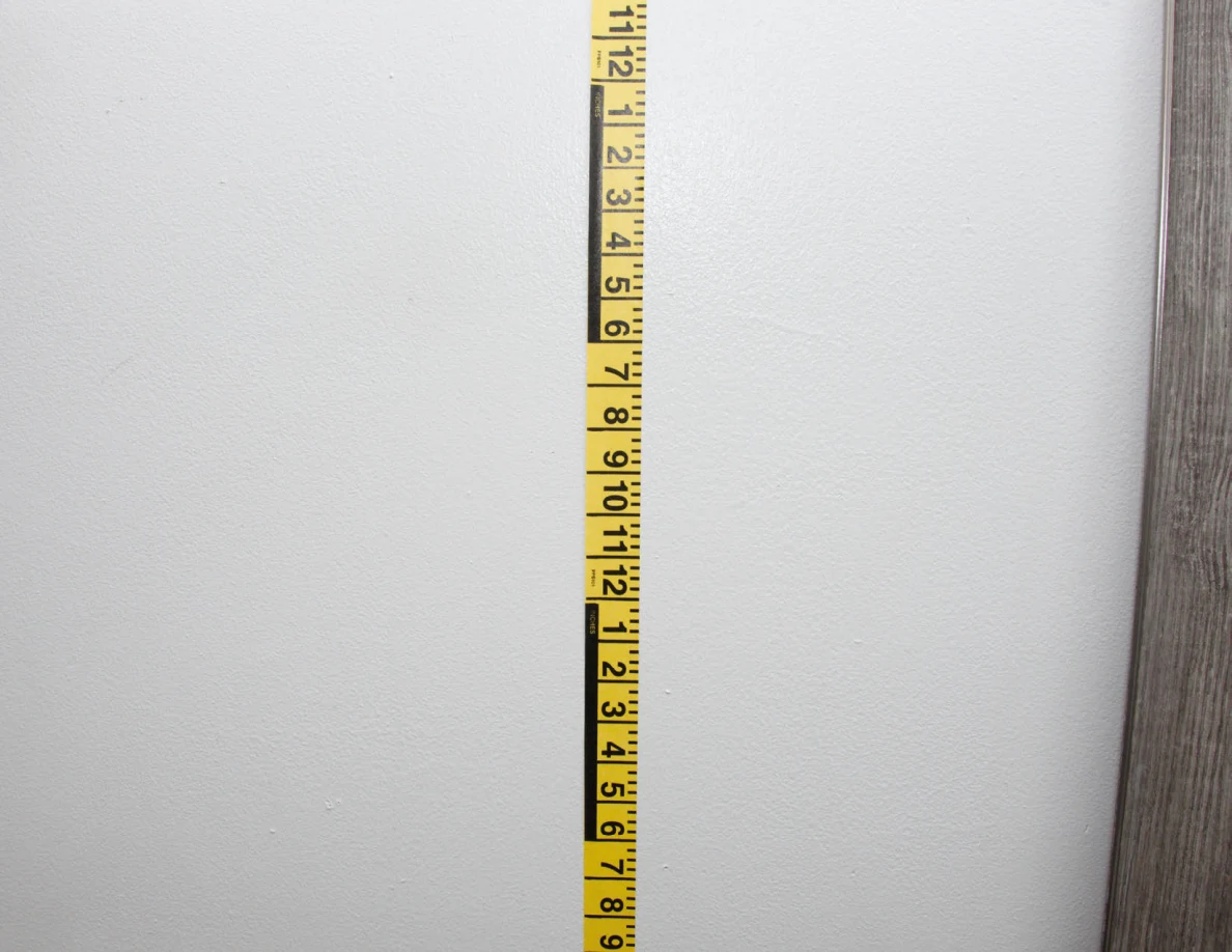 Vertical yellow measuring tape against a pale wall beside a mirror frame.