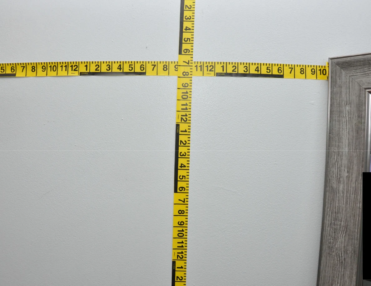 Intersecting yellow measuring tapes across a pale wall.